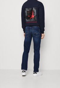 Sudadera navy con diseño gráfico en la parte posterior, combinada con jeans azul oscuro y zapatillas blancas con detalles en negro.