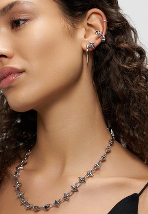 Silberfarbener Schmuck mit Spitzen an einer Kettenhalskette und mehreren Ohrringen, mit einer eleganten, polierten Oberfläche und detaillierter Metallarbeit.