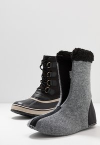 Botín negro impermeable con cordones en la parte delantera y suela de goma, junto a un botín de fieltro gris con acentos negros y forro suave.