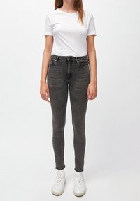 Jeans gris delgados con un lavado descolorido, diseño de cinco bolsillos y una cintura de altura media, combinados con una camiseta blanca sencilla y zapatillas blancas.