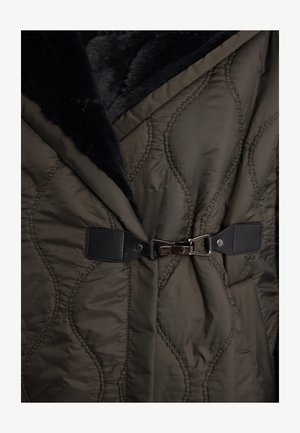 Oliwkowy pikowany płaszcz z miękkim czarnym futerkiem przy kołnierzu, z przodem zamykanym na ciemny skórzany pasek oraz srebrnymi elementami ozdobnymi.