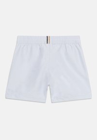 Λευκά σορτς με ελαστική μέση και κάθετες μαύρες και μπεζ ρίγες στο κέντρο της πλάτης, απλωμένα επίπεδα σε λευκό φόντο.