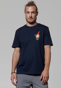 T-shirt en coton bleu marine avec un graphique de gnome sur le côté gauche de la poitrine, col rond, manches courtes et coupe décontractée.