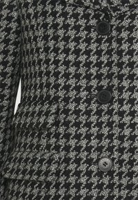 Černý a šedý kabát s vzorem psího zubu z texturované tkaniny, s klopou, dvěma předními kapsami a černými knoflíky.