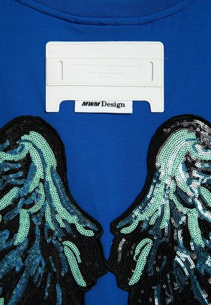 Camiseta de algodón azul con diseños de alas bordados con lentejuelas en aqua y negro. Etiqueta de tela blanca con la marca "MWM Design" en el cuello.
