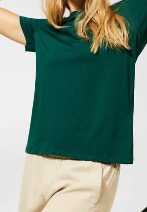 Green cotton t-shirt with short sleeves and a relaxed fit, paired with light beige pants. Simple design, smooth texture, classic shape.