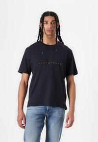 Marineblå t-shirt lavet af bomuld, med rund halsudskæring, korte ærmer og et centralt logo i orange tekst. Glat tekstur og afslappet pasform.