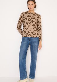 Maglione beige con stampa leopardata marrone, scollo rotondo e maniche lunghe, abbinato a jeans blu a gamba dritta e sneakers chiare.