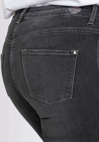 Jeans de mezclilla gris oscuro, con un diseño ajustado que incluye un bolsillo trasero estándar y detalles de costura sutiles. Textura suave, con mínimas embellishments.