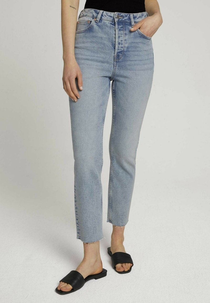 Ljusblå högmidjade jeans med rak passform, som har råa kanter och fem fickor, kombinerat med svarta slidesandaler.