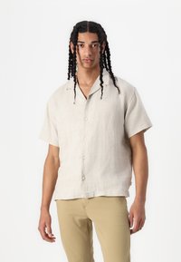 Lichte beige linnen shirt met korte mouwen en een knoopsluiting aan de voorkant, met een ontspannen pasvorm en een subtiele textuurafwerking.