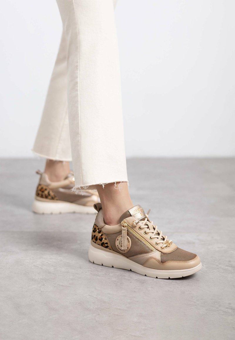 Deportivas de color beige y estampado de leopardo con acentos de malla y cuero, presentan detalles de hardware dorado, suela gruesa y paneles laterales con patrones.