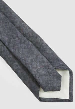 Tamsiai pilka kaklaraištis, pagamintas iš tekstūruotos medžiagos, su lygia balta pamušalu ir smailiu galu; siaura dizaino tinkama formaliam dėvėjimui.