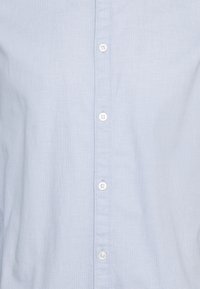 Lichtblauw, geweven overhemd met knopen, voorzien van een textuur, zes witte knopen die langs de voorkant lopen en een klassiek kraagontwerp.