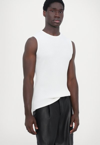 Haut sans manches en maille blanche avec un col rond, associé à un pantalon en cuir noir. Le tissu présente des détails de texture verticaux.