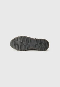 Suela de zapato de goma negra con surcos y patrones texturizados, punta redondeada y un borde suave. Presenta un logo grabado en el centro.