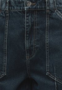 Σκούρο μπλε τζιν από denim με ορατή ραφή, κουμπί με την επιγραφή «MADE NØRGAARD DENMARK» και μπροστινές τσέπες.