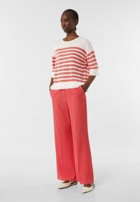 Gestreifter Strickpullover in Weiß und Koralle, kombiniert mit weiten, korallfarbenen Hosen. Bietet eine lockere Passform und eine weiche Textur. Die Schuhe haben eine spitz zulaufende Zehenpartie.