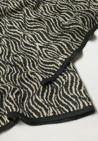 Tissu zébré noir et beige avec des bords froncés et un motif tricoté texturé, présenté sur une surface blanche.