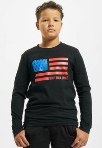 Zwart T-shirt met lange mouwen, voorzien van een rood en blauw Amerikaans vlag graphic en de tekst "LOOP NIET, DANS!" gedrukt in het rood.