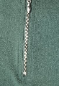 Tessuto verde texture con dettaglio della cerniera argento. Il tessuto presenta un motivo sottile ed è rifinito con cuciture nette lungo la cucitura.