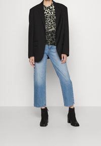Blazer nero oversize, top in stampa leopardata verde e nera, jeans a palazzo blu chiaro e stivaletti neri con tacco a blocco.