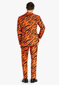 Completo con stampa tigre arancione e nera, caratterizzato da un design slim con vestibilità su misura, tessuto testurizzato e pantaloni abbinati. Scarpe nere completano il look.