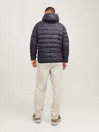 Giubbotto imbottito nero con cappuccio, caratterizzato da cuciture orizzontali e una texture liscia, indossato con pantaloni chiari a fondo elastico.