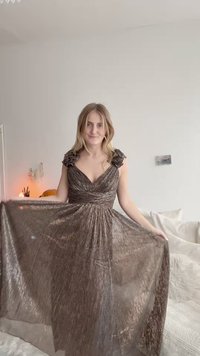 Brązowa, zwiewna wieczorowa sukienka z dekoltem w kształcie litery V i teksturowanym materiałem. Posiada falbany na ramionach oraz wcięcie w talii, sięgającą do podłogi.