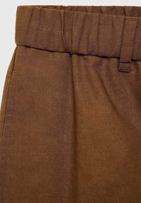 Pantalon en tissu marron avec une taille élastique et une boucle de ceinture visible sur le côté droit.
