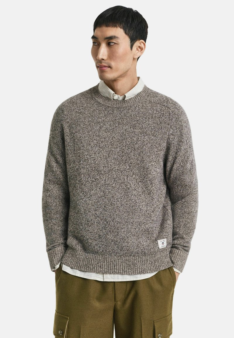 Brauner Strickpullover mit Rundhalsausschnitt, gerippten Bündchen und Saum, strukturiertem Stoff, über einem hellen karierten Hemd getragen, kombiniert mit olivfarbenen Shorts.