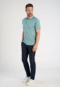 Polo shirt azzurro chiaro con colletto grigio a contrasto, due bottoni, abbinato a pantaloni blu navy e sneakers bianche, creando un look casual.