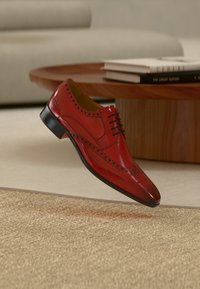 Κόκκινο δερμάτινο παπούτσι με μυτερή μύτη, μαύρα κορδόνια και διακοσμητικές λεπτομέρειες brogue. Μαύρη λαστιχένια σόλα και λεία υφή.