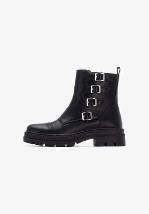 Botas de tobillo de cuero negro con tres correas de hebilla plateada, punta redondeada, suela gruesa y un acabado texturizado.