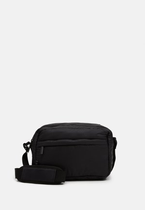 Czarna prostokątna torba na ramię z regulowanym paskiem, przednią kieszenią na zamek i wyściełanym materiałem na jednolitym jasnym tle.