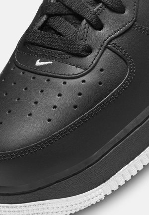 Gros plan sur l'avant d'une basket en cuir noir avec des perforations, des lacets noirs, un logo brodé blanc et une semelle en caoutchouc blanche texturée.