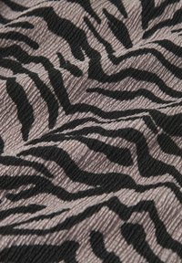 Stoff mit einem Zebramuster, das schwarze Streifen auf einem weichen beigen Hintergrund zeigt, strukturierte Oberfläche mit sichtbaren Rippungen.