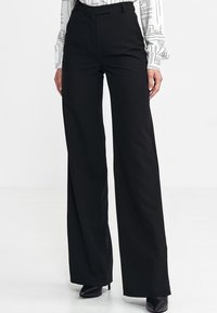 Czarne szerokie spodnie wykonane z gładkiego, tkanych materiału. Posiadają wysoki stan, czyste linie i dopasowany krój. Buty nie są częścią projektu.