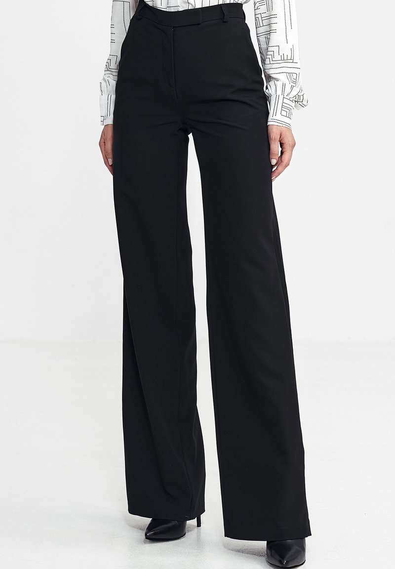 Czarne szerokie spodnie wykonane z gładkiego, tkanych materiału. Posiadają wysoki stan, czyste linie i dopasowany krój. Buty nie są częścią projektu.