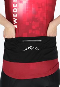 T-shirt de sport rouge et noir avec motif pixelisé, poche dorsale zippée et logo de montagne blanc. Matériau extensible et léger.