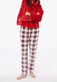 Pullover in morbido velluto rosso con colletto alto, abbinato a pantaloni bianchi con un motivo a quadri nero e rosso. Morbido, accogliente e vestibilità rilassata.
