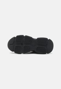 Semelle de chaussure de sport noire avec une surface en caoutchouc texturée présentant un motif en zigzag, offrant une bonne adhérence. Conception durable et flexible.