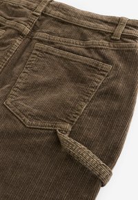 Brune fløjlbukser med lodrette ribber, der har en baglomme og opfoldet kant. Den teksturerede stof fremhæver det ribbede design.
