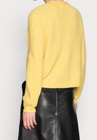 Jersey recortado amarillo con un diseño de punto texturizado, con mangas largas y un escote redondo, combinado con una falda de cuero negro.