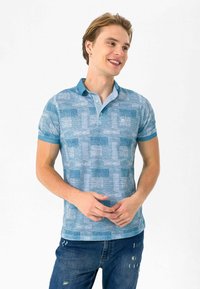 Blå kortærmet polo-shirt med et struktureret mønster, kontrastfarvet krave og kant. Matchet med slidte denimjeans.