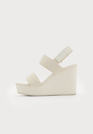 Bēša krāsas wedge sandales ar divām platām siksnām un sašaurinātu papēdi. Izgatavotas no gludas auduma ar teksturētu zoli. Logotips iegravēts papēdī.