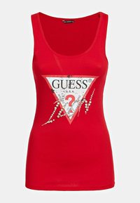 Camiseta sin mangas roja con un gran triángulo de logo de Guess en blanco y rojo y piedras de strass decorativas en la parte frontal.