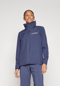 Jachetă impermeabilă Terrex de culoare bleumarin, cu guler înalt, fermoar frontal și manșete elastice. Prezentă branding minimal în partea stângă sus.