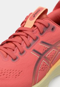 Chaussure de sport rouge avec tige en tissu texturé, système de laçage visible, accents transparents et semelle rembourrée. Logo de la marque sur la languette.