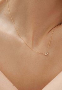 Collar de oro con una delicada cadena que presenta un colgante en forma de copo de nieve adornado con pequeñas piedras blancas, reposando sobre piel desnuda.